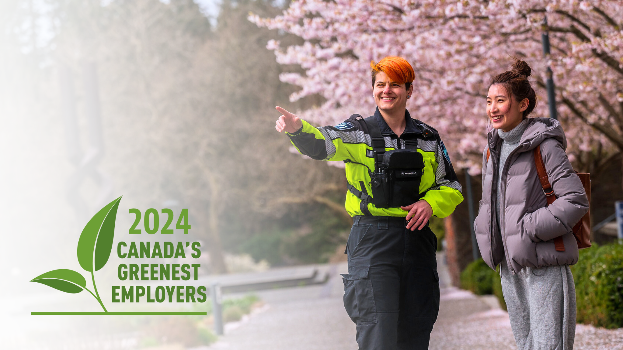 Two people standing in front of cherry blossom trees, one person pointing away | UBC Canada's Greenest Employers 2024
